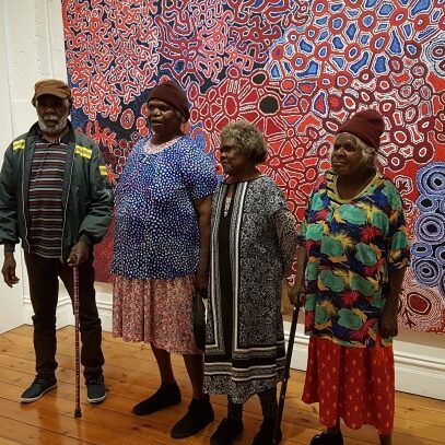 Feature DW curating Artists from the Spinifex Arts Project in Pitjantjatjara lands in Western Australia standing in front of a collaborative map of country.