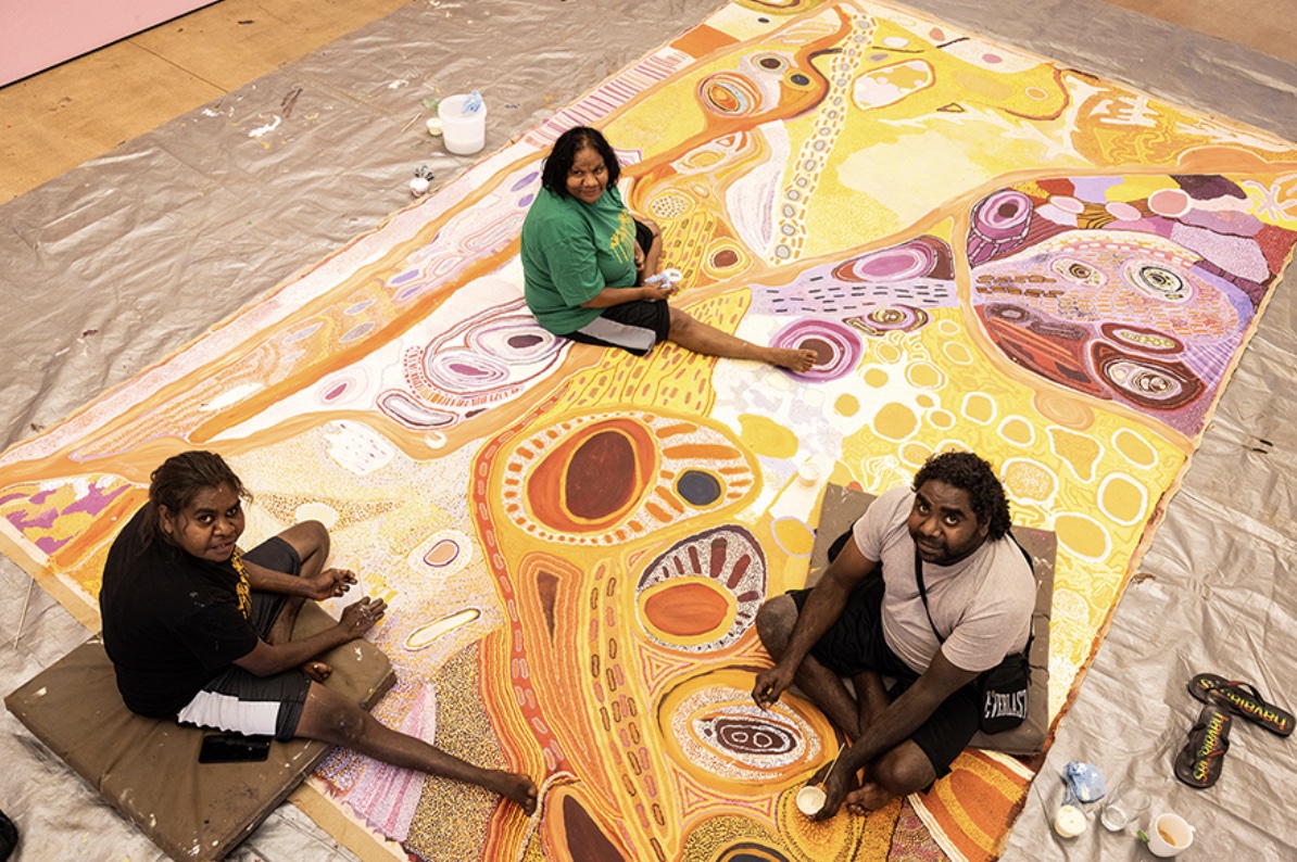Martumili Artists painting on a large colourful canvas